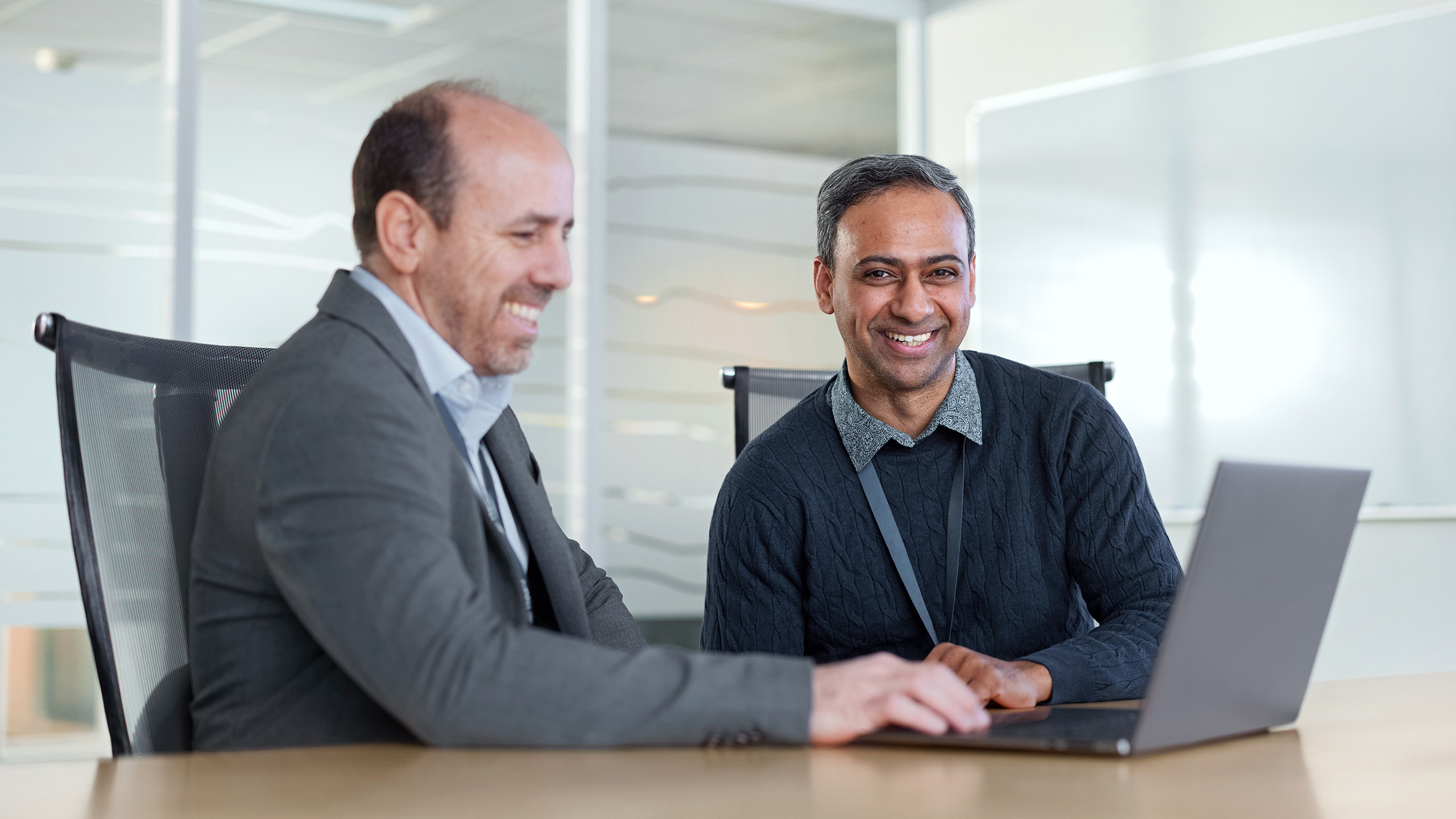 a couple of men sitting at a table looking at a laptop