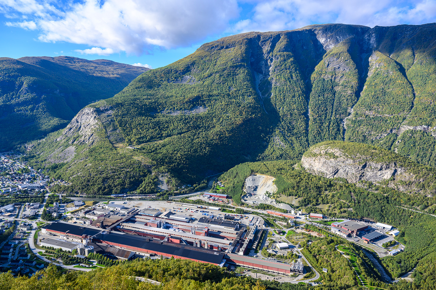 a large green mountain with buildings and trees