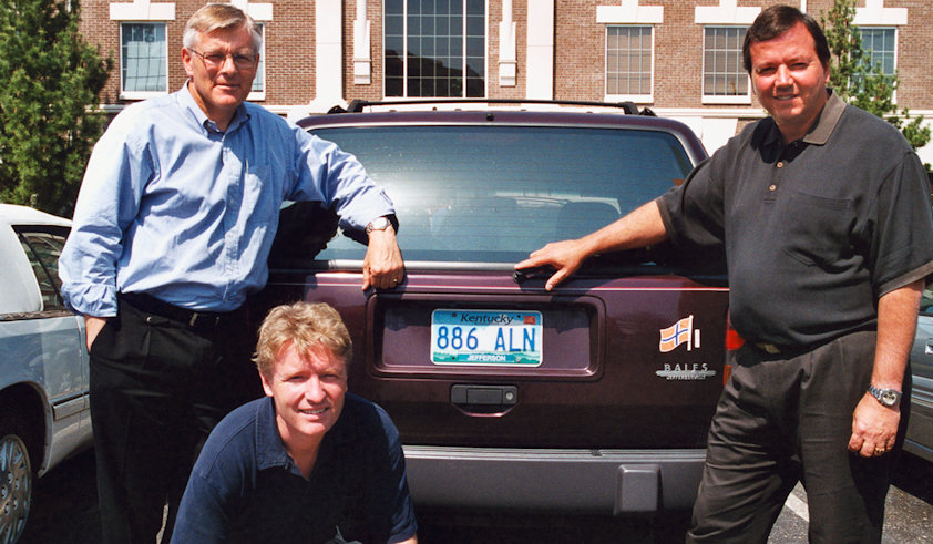 a group of people posing for a photo in front of a car
